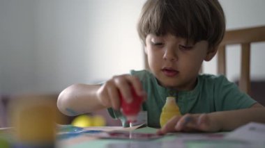 Evde boya yapmak için boya fırçası kullanan küçük bir çocuk. Evde çocuk yaratıcılığı sanatsal aktivitesi. Çocuk boyama 