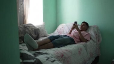 Gevşemiş bir İspanyol adam yatakta uzanıp cep telefonu ekranına bakıyor. Genç bir Güney Amerikalı odada telefon tutuyor.