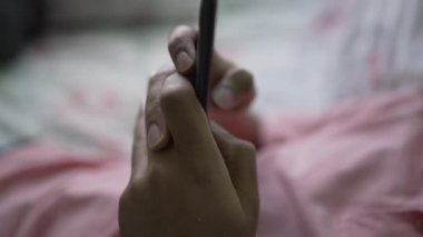 Yatakta uzanmış, yatak odasında cep telefonuyla yazı yazan bir adam.