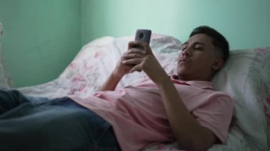 Yatakta telefonu tutan sıradan bir İspanyol. Rahatlamış insan akıllı telefon aygıtı ekranına bakarak uzanıyor