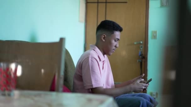 ソファに座って電話を使っているひとりのヒスパニック系の男 スマートフォンを持っているラテン語の人 — ストック動画
