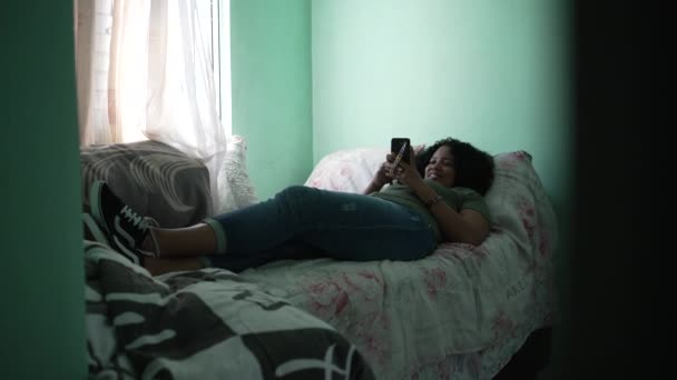 一名巴西年轻女子躺在床上用智能手机发短信 — 图库视频影像