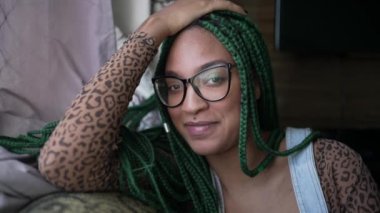 Saç örgülü, kameraya gülümseyen bin yıllık bir kız. Bir genç siyah Latin kadın portresi kanepede oturuyor.