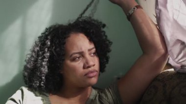 Düşünceli bir Afrikalı Amerikalı kadın dalgın dalgın kıvırcık saçlarıyla oynuyor.