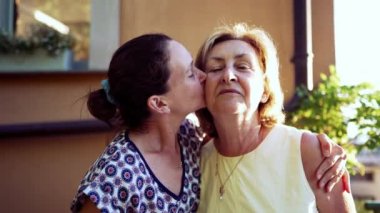 Neşeli yetişkin kız, yaşlı anneyi yanağından öpüyor. Aile bağlarını güçlendiren bir ilişki. İki farklı nesil kadın.