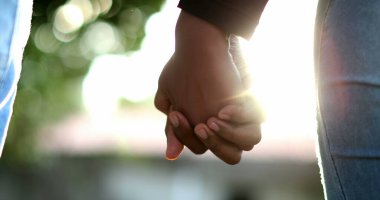 Arka planda güneş ışığının parlamasıyla birleşen ellerin yakın çekimi. İki aşık arasındaki güzel romantik an