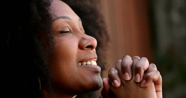 African woman closing eyes in prayer outside