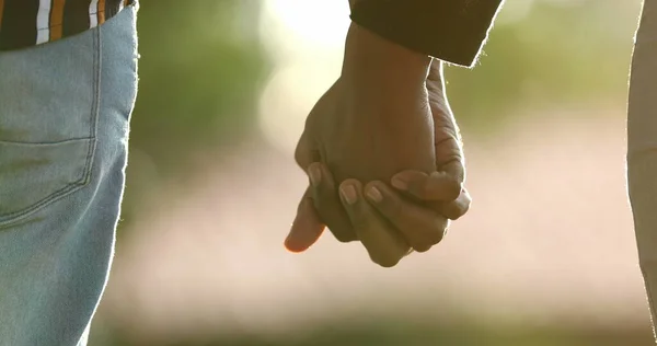 Close-up of hands joining together with sunlight flare in the background. Beautiful romantic moment between two lovers