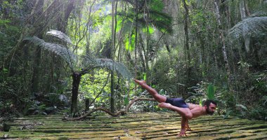 Yogi adam, tropik ormanın ortasında amuda kalkarak yoga eğitimi veriyor.