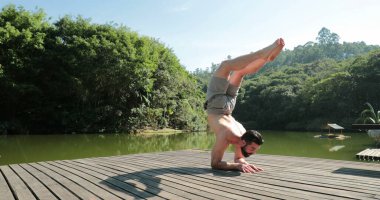 Doğada yoga pratiği yapan biri. Asana 'da amuda kalkan genç bir adam.