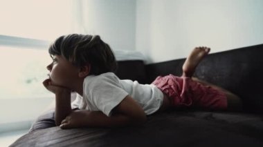 Kanepede uzanmış, kameradan çizgi film izleyen küçük bir çocuk. Rahat bir çocuk kanepeye uzandı.