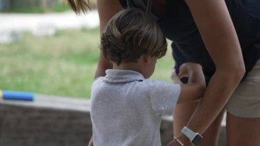 Anne dışarıdaki küçük oğlundan çocuk gömleği çıkarıyor. Anne ve babası dışarıda çocuk kıyafetlerini çıkarıyorlar.