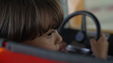 Lunaparkta elinde direksiyonla araba sürüyormuş gibi yapan dalgın, küçük bir çocuğun arkası. Düşünceli duygu.