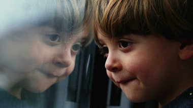 Düşünceli bir çocuk trenin camına yaslanıyor. Yüksek hızlı tren ile seyahat eden küçük çocuğun ayna camı yansıması. Düşünceli çocuk manzarayı seyrediyor.