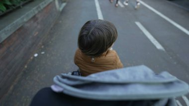 Bebek arabasında oturan çocuk. Ebeveyn karakteri, yeni yürümeye başlayan oğluyla şehir caddesinde yürüyor. Anne bebek arabası bakış açısını zorluyor.