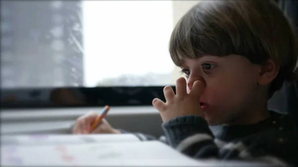 Concentrated Child nose picking while doing homework seated inside on a moving train