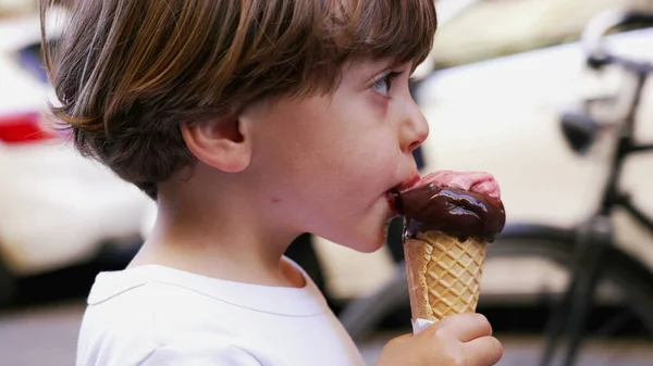 Young boy eating ice cream cone outside. Child eats italian gelato outdoors during summer day