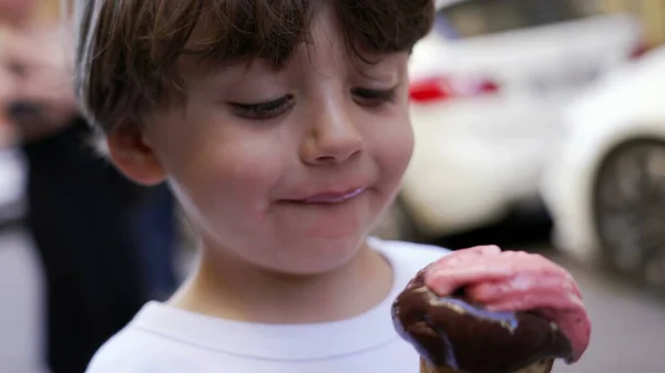 One little boy eating icecream outside. Portrait face closeup of a chile holding italian ice cream dessert during vacations