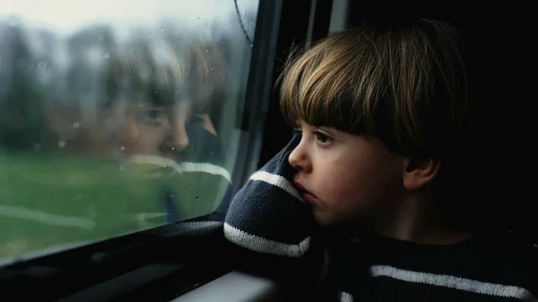 Thoughtful child staring at train window feeling sadness. Pensive passenger boy traveling in modern transportation during gray moody day