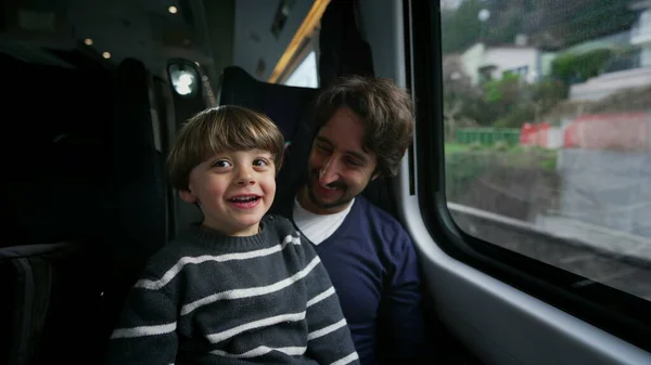 Happy father and son traveling together by train during vacation holidays. Little boy pointing with hand at landscape passing by inside transportation in motion