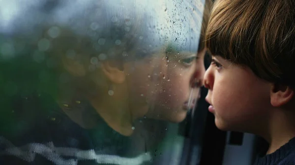 Pensive child leaning on moving train window looking at landscape. Small boy travels on transportation