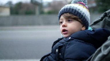 Çocuk kış mevsiminde gezintiye çıkmış. Koyu giysili, bereli ve ceketli çocuk.