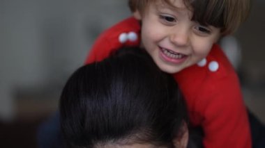 Küçük çocuk annesinin sırtına biniyor. Otantik gerçek ebeveyn ve çocuk ilişkisi gülüyor ve gülümsüyor. Anne ve çocuk kucaklaşır