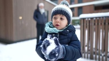 Heyecanlı küçük bir çocuk aralık ayında taze kış mevsiminde havadan neşeyle atlıyor. Şapka ve eşarp giyen bir çocuk.