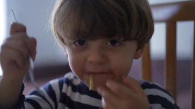 Çocuk tek başına spagetti yiyor. Küçük bir çocuk çatalla erişte yiyor.