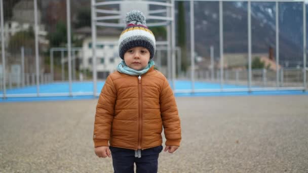 冬天的时候 小男孩穿着便帽围巾和夹克站在公园外面 多愁善感的幼儿穿着保暖的衣服站在户外 — 图库视频影像