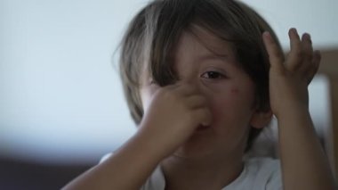 Gözü yaşlı küçük bir çocuk yüzünü kapatıyor. Üzgün çocuk yorgun düşünceli bir ifadeyle