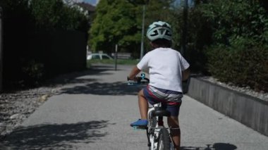 Aktif bir çocuk dışarıda kask takarak bisiklet sürüyor. Çocuk bisikletçi güneşli bir günde dışarıda egzersiz yapıyor.