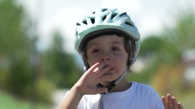Üzgün küçük bir çocuk yüzünü kapatıyor. Kasklı, dışarıda bisiklet süren mutsuz bir çocuğun portresi.