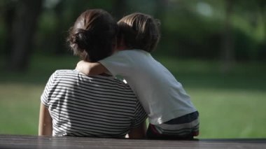 Parkta annesini kucaklayan bir çocuk. Küçük çocuk güneşli bir günde ebeveyni kucaklıyor.