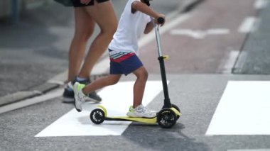 Çocuk, scooter 'ı zebra hattında karşıdan karşıya geçiyor. Güneşli bir günde aile ve çocuk yaya geçidinde. Aktif küçük çocuk kaldırımdan karşıya geçiyor.