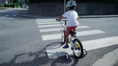 Genç bisikletçi yaya geçidi zebra hatlarında karşıdan karşıya geçiyor. Çocuk dışarıda tekerlek ve kaskla bisiklet sürüyor. Sportif çocuk şehirde egzersiz yapıyor.