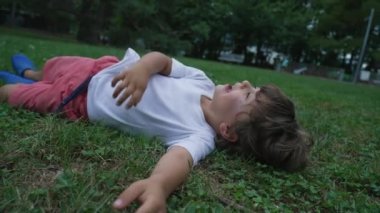 Mutlu bir çocuk çimlere uzanmış gülümsüyor ve gülüyordu. Parkta yatan erkek çocuğun yüzünü kapat.