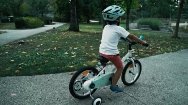 Çocuk parkta koruyucu kask takarak bisiklet sürüyor. Dışarıda tekerlekli bisiklete binen sportif bir çocuk. Aktif çocuk egzersiz yapıyor.