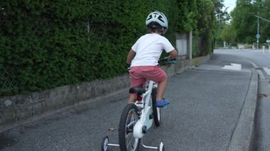 Şehir kaldırımında bisiklet süren küçük bir çocuk. Bisiklete binen çocuklar sokakta kaskla gezerler.