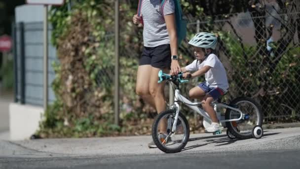 子供の自転車通りで母親と交差する クロスウォークで子供を助ける親 車輪の上にヘルメットをかぶって — ストック動画