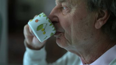 Sabah kahvaltısında kahve içen kıdemli bir adam. Yakın çekim yaşlı insan yüzü yudumlayan kafe