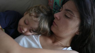 Anne ve çocuk evdeki kanepede yatarak kucaklaşırlar. Anne şefkati ve küçük çocuk sevgisi.