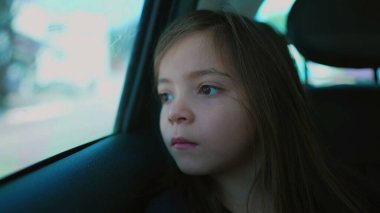 Arabanın arka koltuğunda dalgın küçük bir kız. Düşünceli bir çocuk. Kapalı bir yüz. Araç camından dışarı bakıyor.