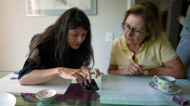 Yetişkin kız, yaşlı anneye cep telefonu cihazıyla bilgi veriyor. Üst düzey bir kadına akıllı telefon gösteren kişi