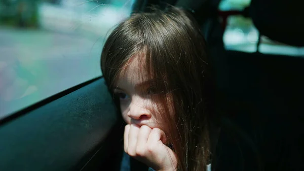 Portrait of a bored sleepy child feeling bore and sadness. Sad little girl closeup face traveling by car leaning on car window backseat