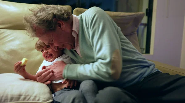 Grandfather and grandchild relationship. Grandparent hugging grandson in living room couch at night. Grandpa embraces grandchild