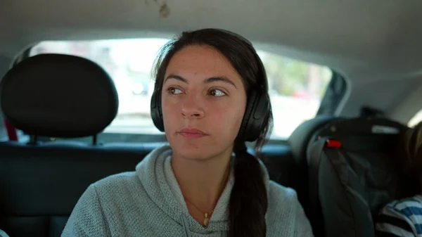 Person in car backseat listening to music podcast or audiobook on headphones. Woman traveling on road with noise cancelling audio headphone inside vehicle transportation