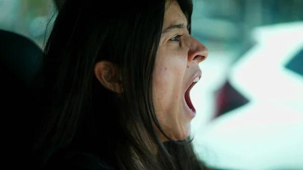 Sleepy driver yawning closeup face. Exhausted woman driving on road yawns