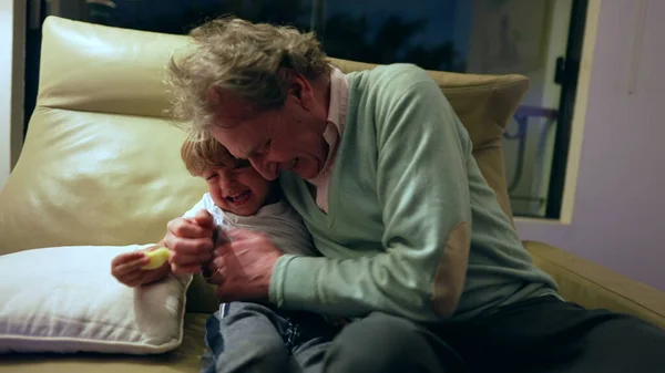 Grandfather and grandchild relationship. Grandparent hugging grandson in living room couch at night. Grandpa embraces grandchild