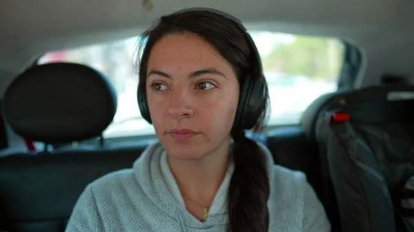 Person in car backseat listening to music podcast or audiobook on headphones. Woman traveling on road with noise cancelling audio headphone inside vehicle transportation